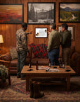 Three men in a rustic living room pointing at a Basset Hound-Heritage History Portrait on the wall.
